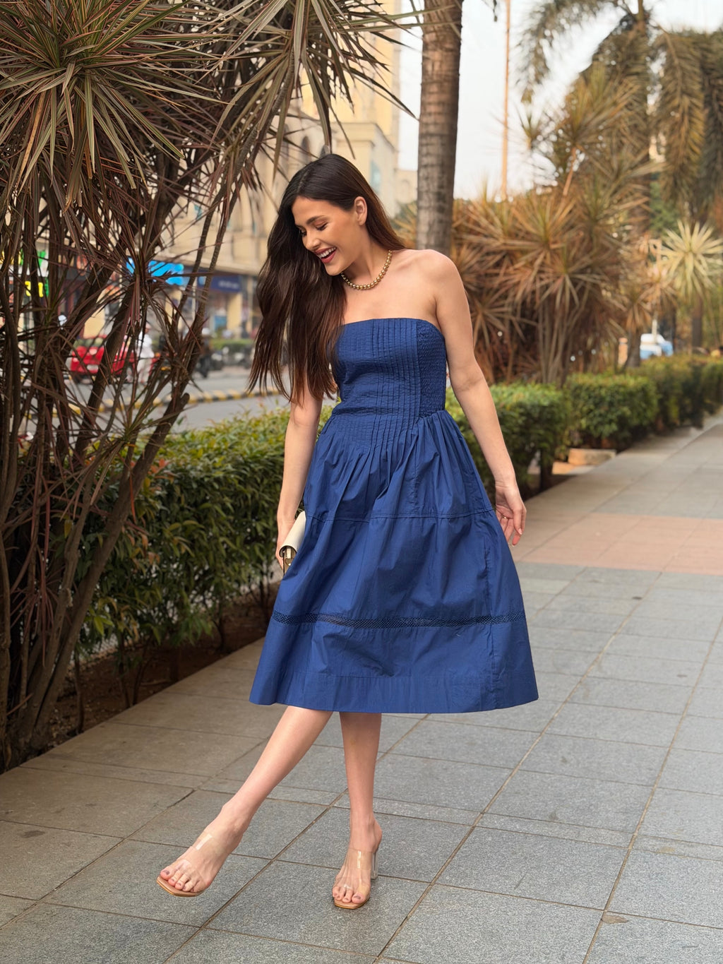 Woman in a blue strapless dress walking on a sidewalk with plants and buildings in the background, western midi dress