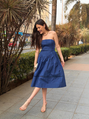 Woman in a blue strapless dress walking on a sidewalk with plants and buildings in the background, western midi dress