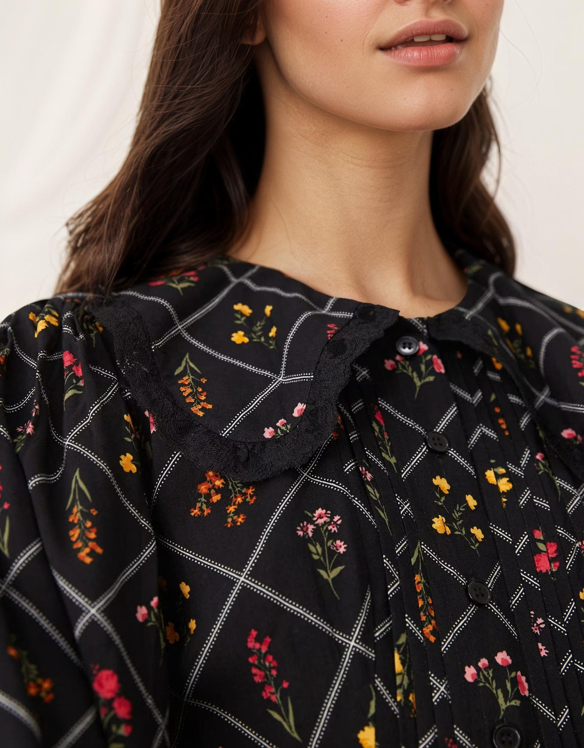 Close-up of a woman wearing a black dress with floral patterns on a white background