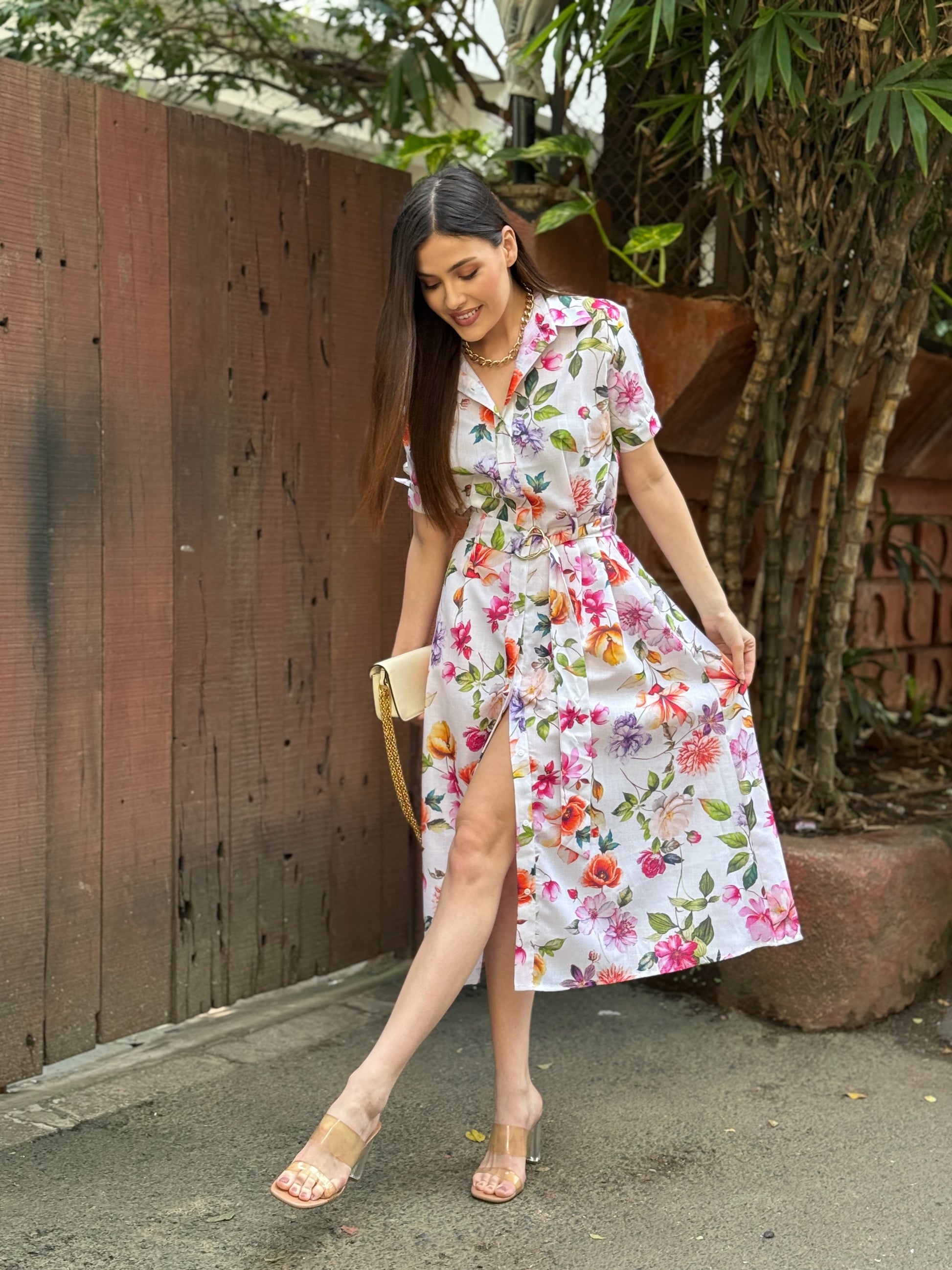 Woman in a floral dress standing outdoors next to a wooden fence.