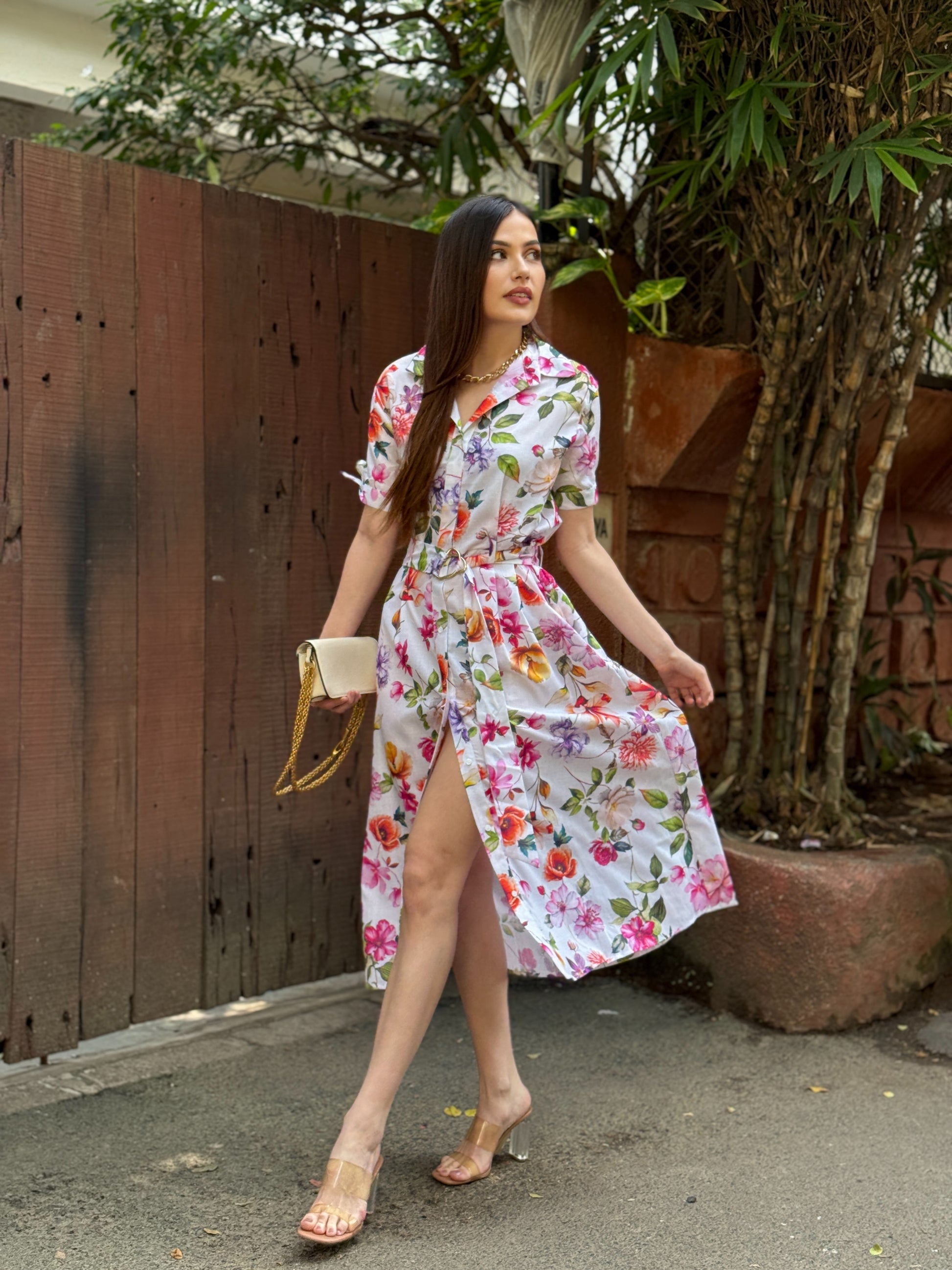 Woman in a floral dress walking outdoors with a wooden fence and tree in the background
