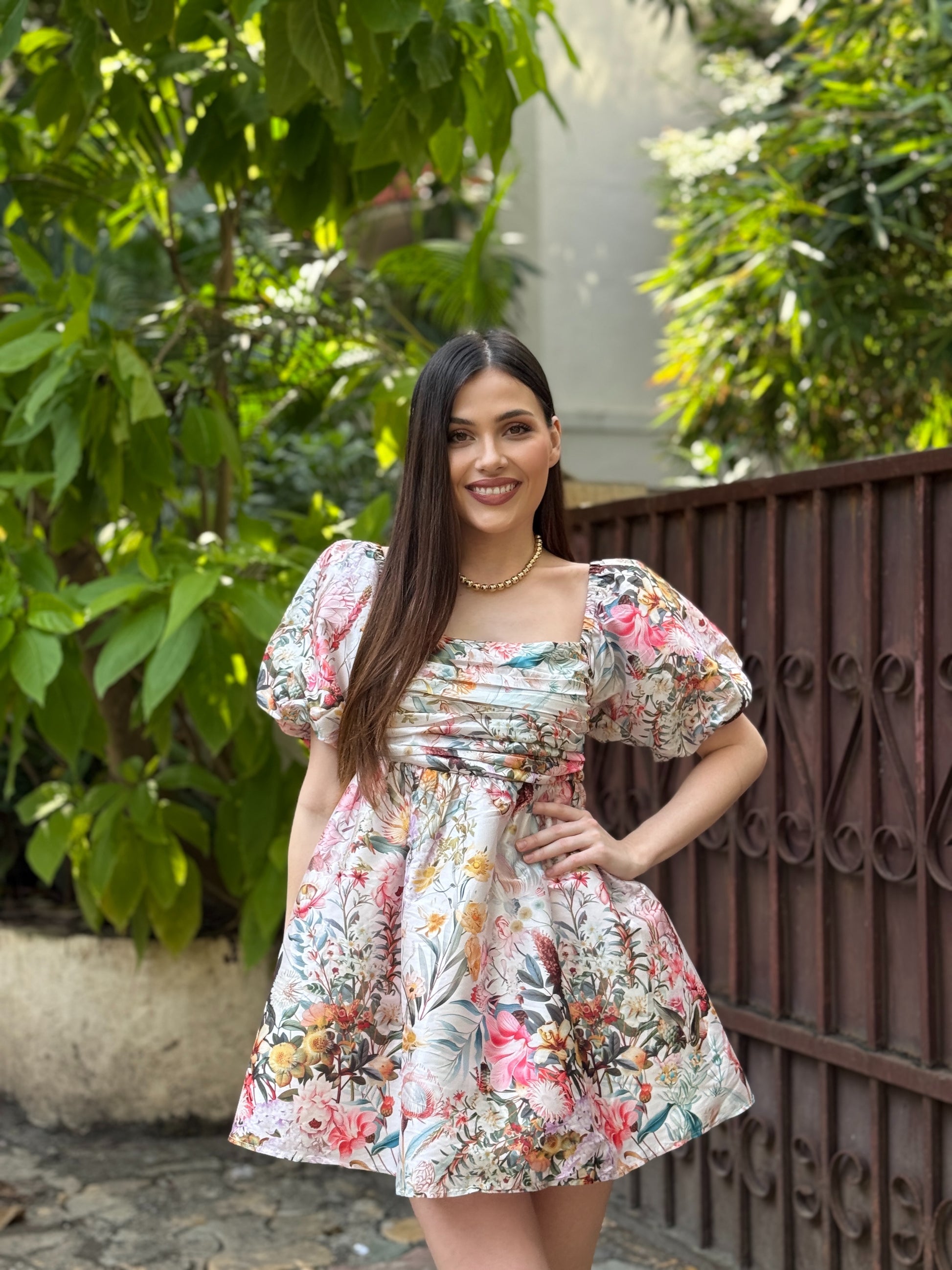 Woman in a floral dress standing outdoors with greenery in the background