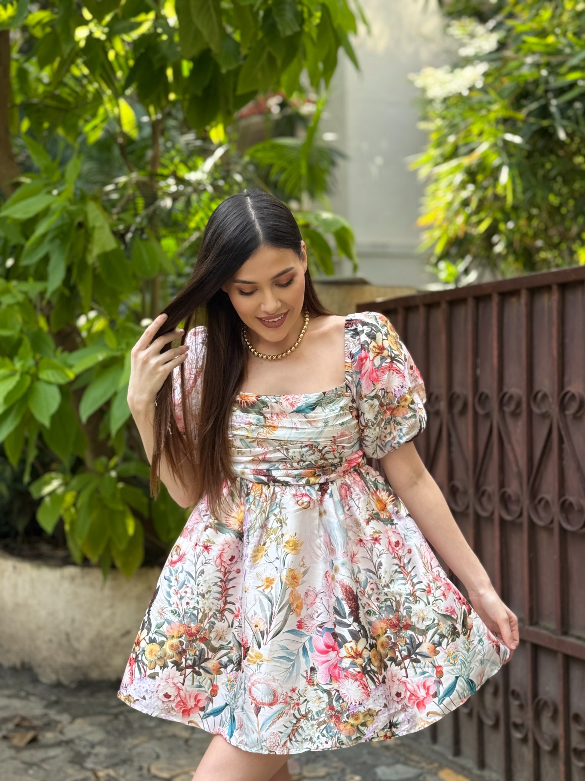 Woman in a floral dress standing outdoors with greenery in the background
