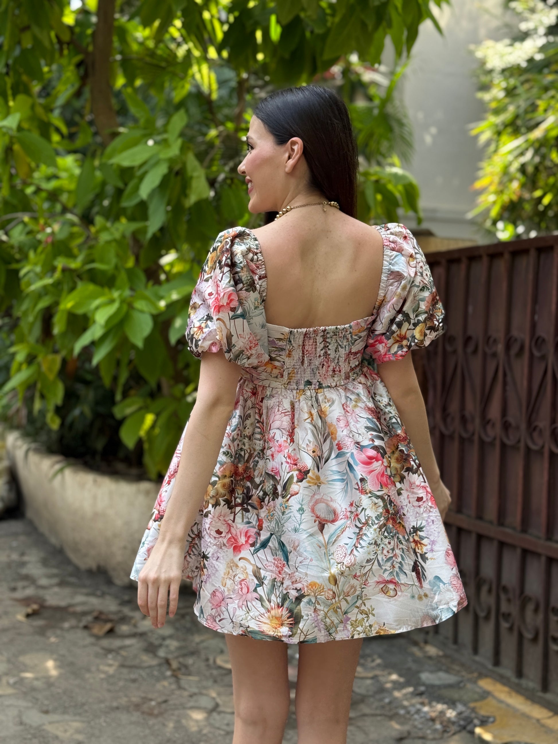 Woman wearing a floral dress standing outdoors with greenery in the background, summer dress