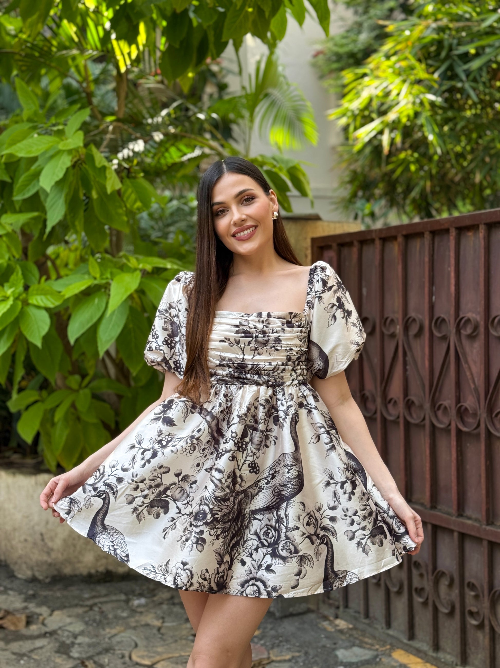 Woman in a floral dress standing outdoors with greenery in the background, peacock design dress