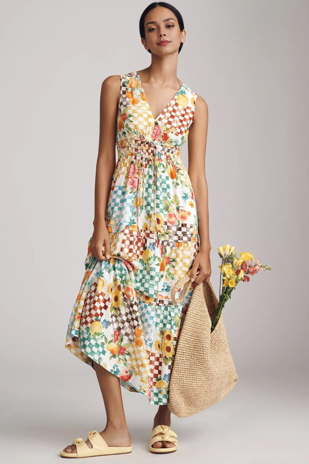 Woman wearing a colorful patterned dress holding a straw bag and flowers on a plain background. colorful maxi dress for summer. fruity design